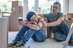 Moving house: Couple taking a break, sitting in room filled with cardboard boxes