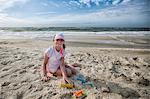 Girl sitting on beach playing in sand, looking at camera smiling