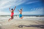 Rear view of girl and boy on beach arms raised jumping in mid air