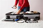 Woman packing suitcase, holding smartphone, mid section