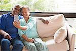 Senior couple sitting on sofa, taking self portrait using smartphone