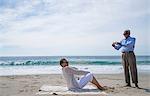 Senior couple on beach, man taking photograph of woman using smartphone