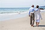 Senior couple waking on beach, rear view