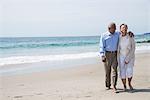 Senior couple waking together on beach, smiling