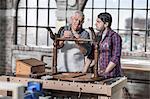 Senior craftsman demonstrating restoration to trainee in antique restoration workshop