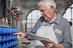 Senior craftsman with digital tablet selecting components in antique restoration workshop