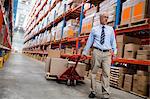 Warehouse manager walking in aisle with a pallet truck