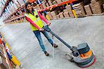 Woman cleaning warehouse floor with machine