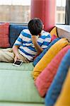 Upset boy sitting on sofa and holding a mobile phone