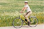 Senior woman vigorously exercising. She's cycling on a country road by the fields.