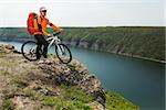 Cyclist in Orange Wear Riding the Bike Down Rocky Hill under River. Travel Concept