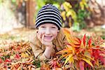 cool serious little boy enjoying time outdoors at beautiful autumn park and holding bouquet of colorful leaves