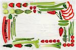 Red and green fresh health food border with vegetable and fruit selection over distressed white wood background. High in vitamins, antioxidants, minerals and anthocyanins.
