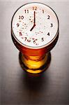 clock symbol on foam in beer glass on black table, view from above