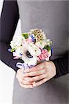 Woman in grey dress and black shirt is holding a spring bouquet from pink tulips, violet grape hyacinths, white anemones, violet veronica and white buttercup with violet ribbon