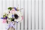 Pastel bouquet from pink tulips, violet grape hyacinths, white anemones, violet veronica and white buttercup with violet ribbon with white wooden shutter background