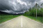 Asphalt road to the mountains under the dramatic stormy sky.