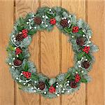 Christmas wreath with holly, mistletoe, pine cones and snow covered blue spruce fir over oak wood front door background.