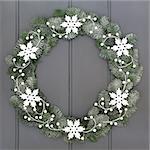 Christmas white snowflake wreath decoration with snow covered blue spruce fir and decorative mistletoe  over grey front door background.