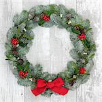 Traditional christmas wreath decoartion with holly, fir and mistletoe over distressed white wood front door background.