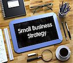 Small Business Strategy - Text on Small Chalkboard.Small Business Strategy - Blue Small Chalkboard with Hand Drawn Text and Stationery on Office Desk. Top View. 3d Rendering.