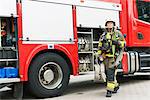 Sweden, Female firefighter with equipment standing next to fire truck looking up