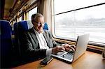 Sweden, Mature man typing on laptop while traveling on train