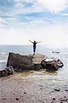 Estonia, Woman with raised arms standing on rock at seaside