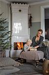 Sweden, Mother and daughter (6-7) sitting by fireplace opening Christmas presents