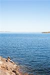 Sweden, Uppland, Runmaro, Barrskar, Boy (6-7) sitting on rock by sea