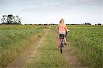 Sweden, Skane, Soderslatt, Beddinge, Blonde girl (10-11) riding bike along dirt road in green field