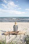 Sweden, Skane, Soderslatt, Beddinge, Mature woman sitting on driftwood and looking at sea
