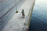 Sweden, Sodermanland, Stockholm, Sodermalm, Slussen, Mid adult man with bicycle standing on river bank