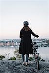 Sweden, Sodermanland, Stockholm, Sodermalm, Skinnarviksberget, Rear view of young woman standing by bicycle on rock