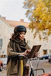 Sweden, Uppland, Stockholm, Vasastan, Rodabergsbrinken, Young woman using digital tablet standing by bicycle