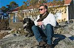 Finland, Pohjanmaa, Luoto, Man sitting with dog on rocks in front of house