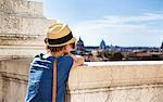 Young woman from behind, leaning on a low wall, and the city of Rome