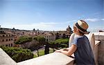 Young woman from behind, leaning on a low wall, and the city of Rome