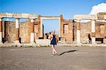 Young woman tourist, back, look at a map while walking in the ruins of Pompeii