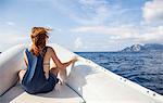 Young woman from behind, contemplates the island of Capri, in front of a boat