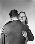 1950s 1960s WOMAN EMBRACING HUGGING MAN WITH HIS BACK TO CAMERA