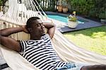 Young man reclining on garden hammock with hands behind his head