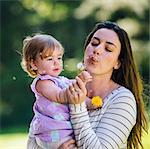 Woman and toddler daughter blowing dandelion clock in park
