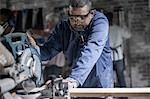 Carpenter sawing plank of wood in workshop