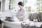 Woman using laptop on sofa beside pet dog