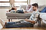 Young couple relaxing at home, young woman sleeping on sofa, young man using laptop