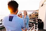 Young man photographing girlfriend at dusk with smartphone on pier, Santa Monica, California, USA