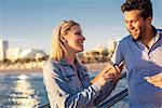 Young couple reading smartphone text on pier, Santa Monica, California, USA