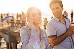 Young couple on sunlit pier chatting on smartphone, Santa Monica, California, USA