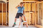 Portrait of cute boy sitting on top of a step ladder in unfinished room